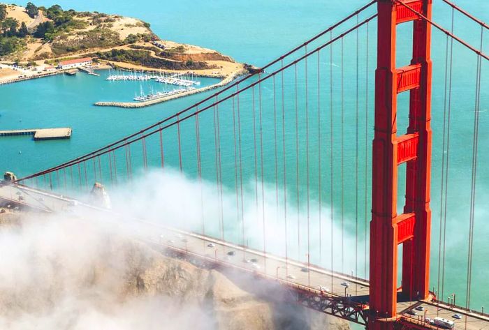 An aerial perspective of a large metal red bridge spanning a bay, enveloped in low-hanging clouds.