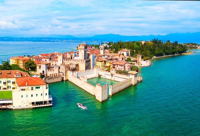 A breathtaking panoramic view of a stone fortress overlooking a turquoise lake, surrounded by the historic buildings of a town on a lush island.