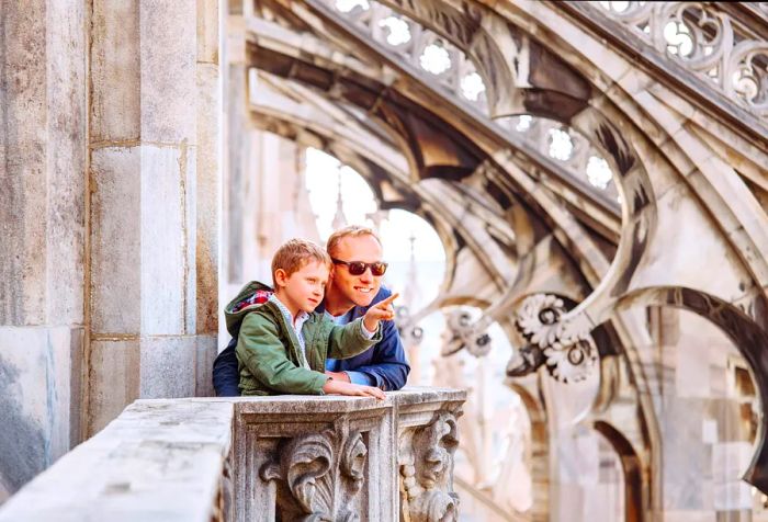 A son points out something to his father while they stand on the stunning rooftop terrace of a grand church.