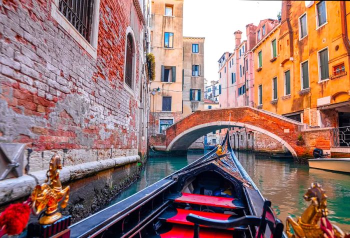 A gondola glides by, offering views of an arch bridge spanning a canal nestled between tall buildings.