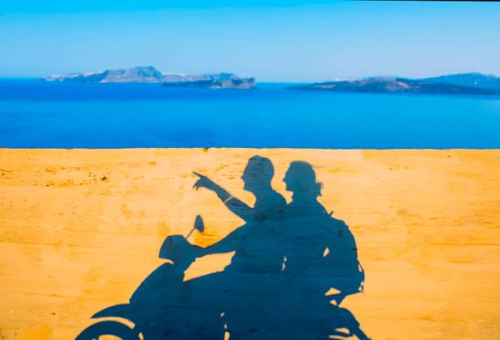 The silhouette of two people on a motorbike against the backdrop of the blue sea.