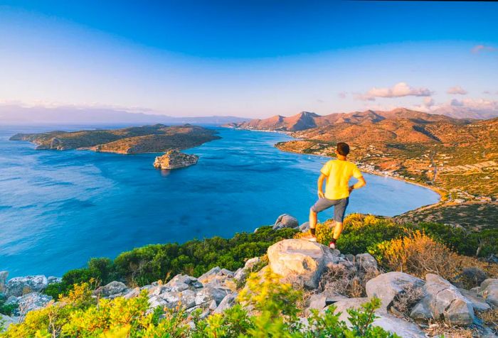 A man in a yellow shirt stands on a rock, admiring the breathtaking view of a bay surrounding an island.