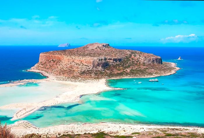 A remote, uninhabited rock island boasting a strip of white sandy beach embraced by crystal-clear blue waters.