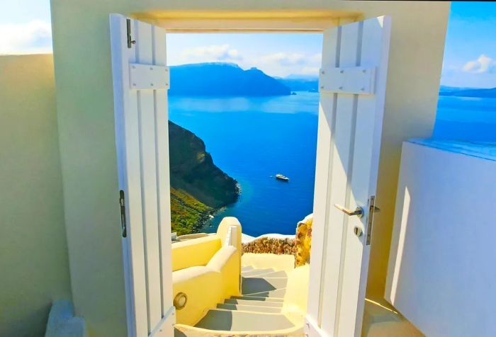 A white door opens to a staircase that offers stunning views of a cruising boat gliding across the vast ocean.