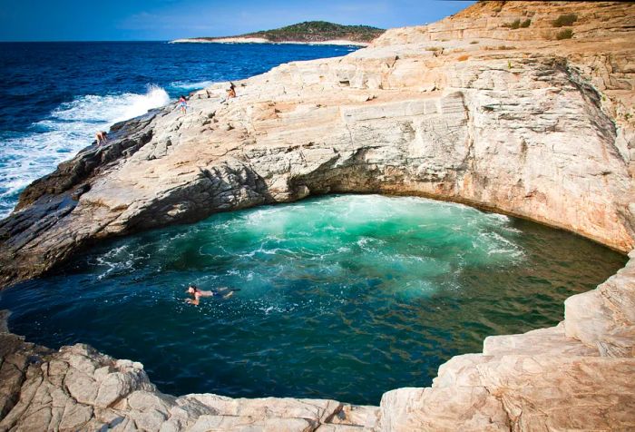 A person enjoys a swim in a natural rock pool adjacent to the ocean with tumultuous waves.