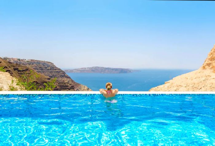 A woman relaxing in a swimming pool with a view of rocky islands and the serene blue sea.