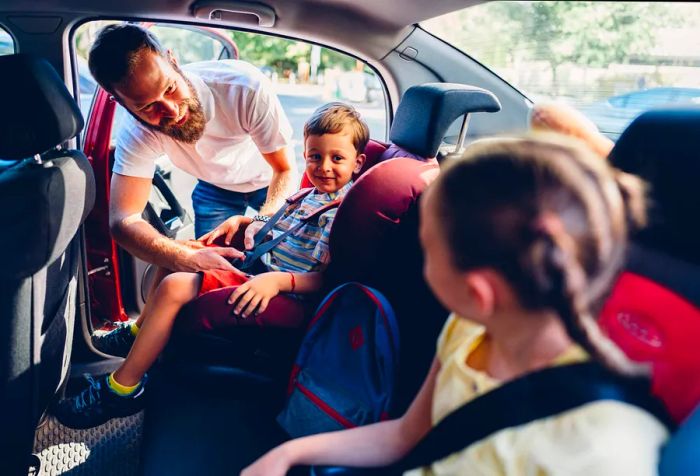 A father assists his kids in settling into their booster seats before the trip begins.