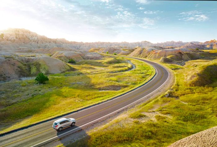 A silver vehicle navigates a road winding through hilly terrain.