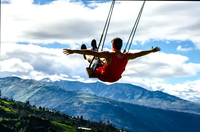 A person swinging on the 'Swing at the End of the World' with mountains in the background.