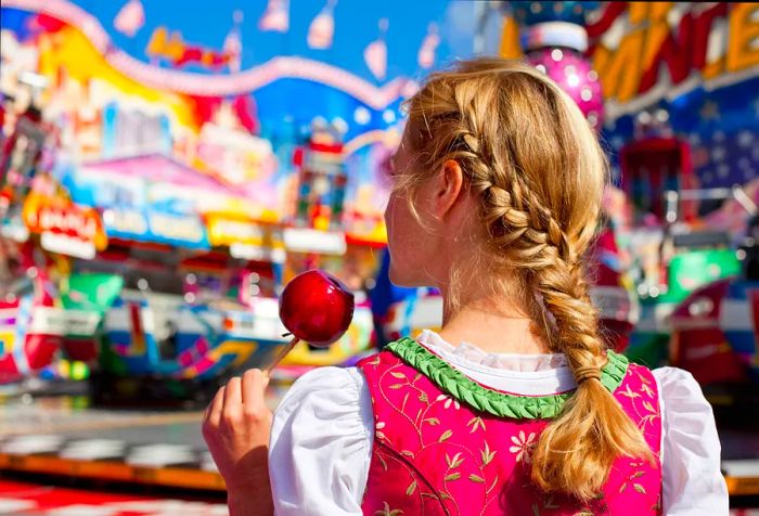 A blonde girl with braided hair enjoying a sugar-coated apple on a stick.