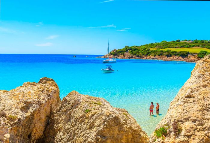 Two men standing knee-deep in the turquoise water, gazing at the boats in the distance.