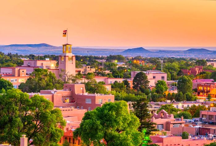 A tower adorned with a flag rises above a residential area surrounded by lush trees beneath a vibrant orange sky.