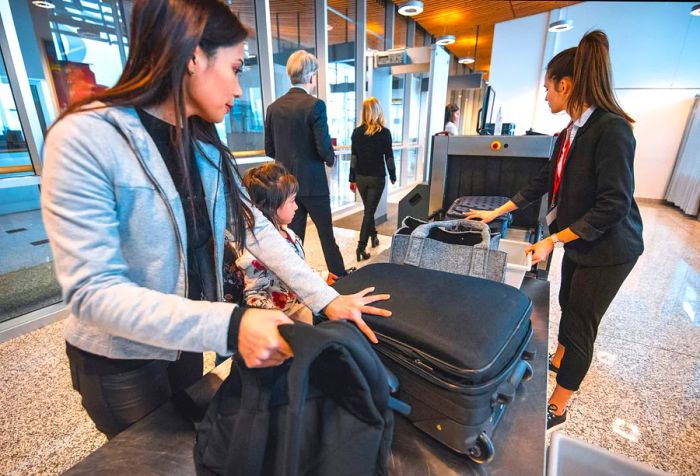 A mother and daughter wait at an airport for their luggage as it exits the X-ray machine.