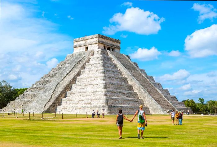 A couple of tourists posing in front of the iconic El Castillo temple at Chichen Itza, Yucatan, Mexico.