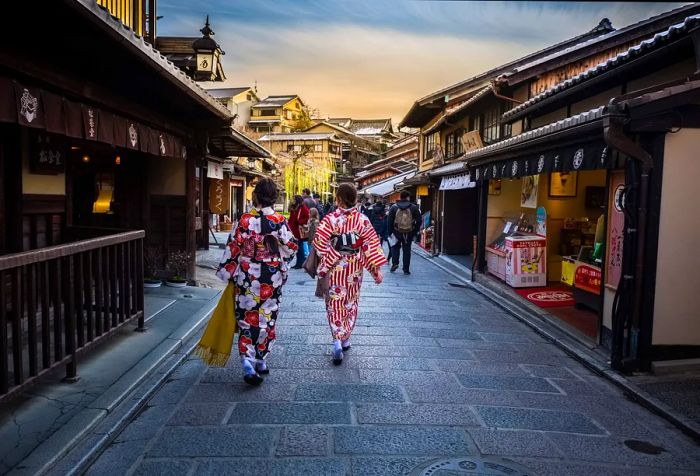 Two women in colorful floral kimonos strolling down a lively street lined with traditional houses.