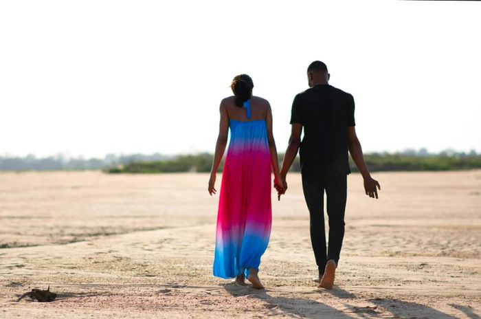 A couple strolling barefoot along a beach in Nigeria