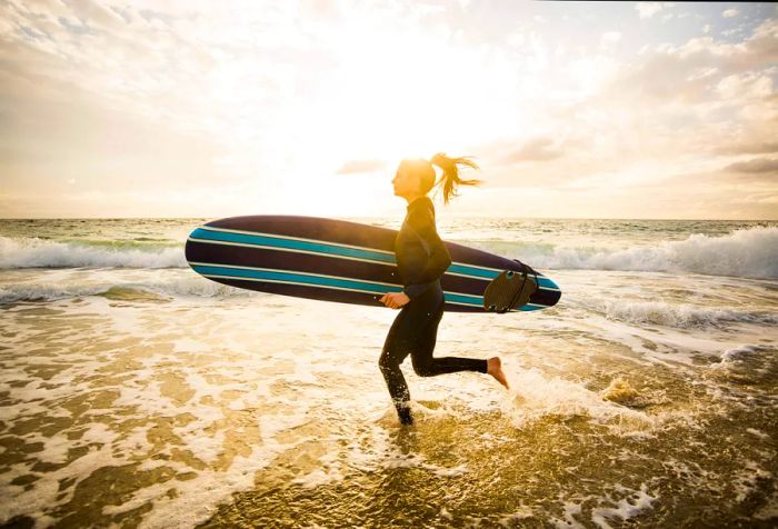 A female surfer dashes toward the ocean, her surfboard tucked under her arm.