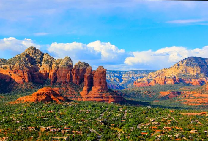 Homes nestled among lush evergreen trees set against a stunning backdrop of red rock formations.