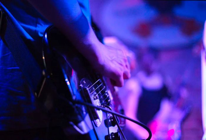 A hand strums an electric guitar illuminated by blue lights.