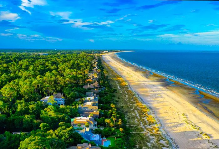 An aerial view showcasing modern luxury beach homes on a lush island with sandy shores and the calm blue sea surrounding it.