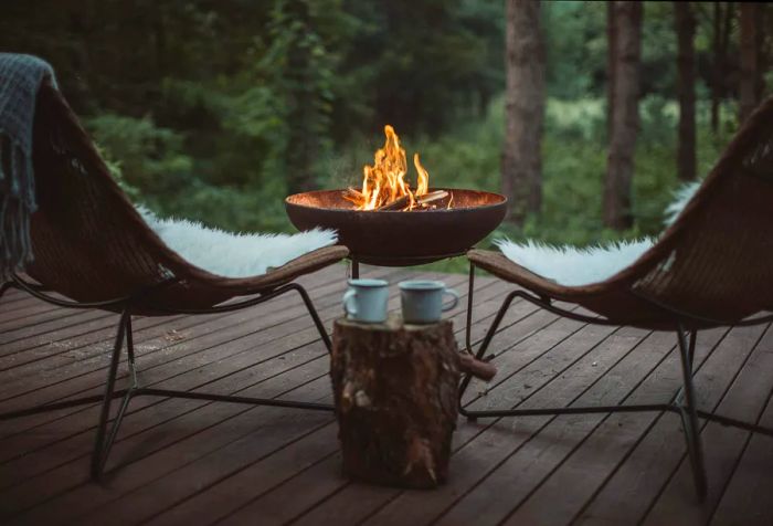 A charming wooden porch with two comfy chairs surrounding a campfire, overlooking a vibrant forest.