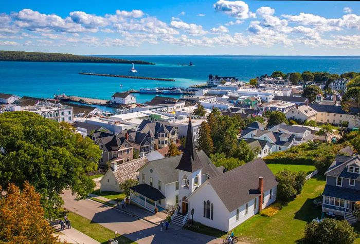 A white lighthouse stands proudly in the center of a channel, close to a charming seaside village.