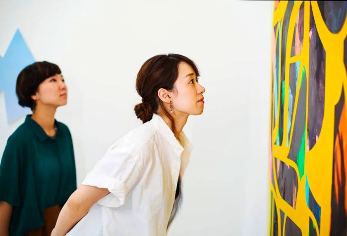 A woman in a white shirt gazes intently at a piece of abstract art on the wall.