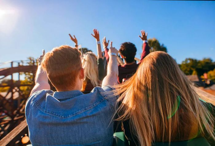 Riders on a roller coaster enthusiastically throw their hands in the air.