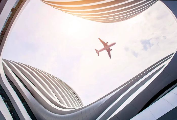 An airplane soaring through the sky, framed by the elegant curve of a building.