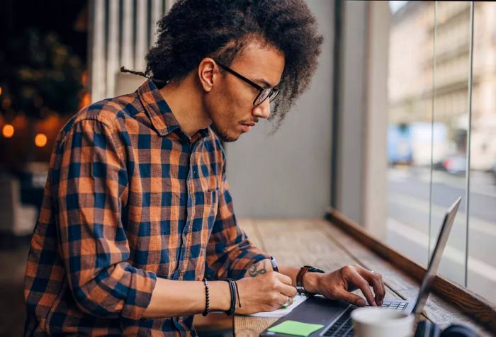 A young man typing on his laptop at a coffee shop, immersed in his work.