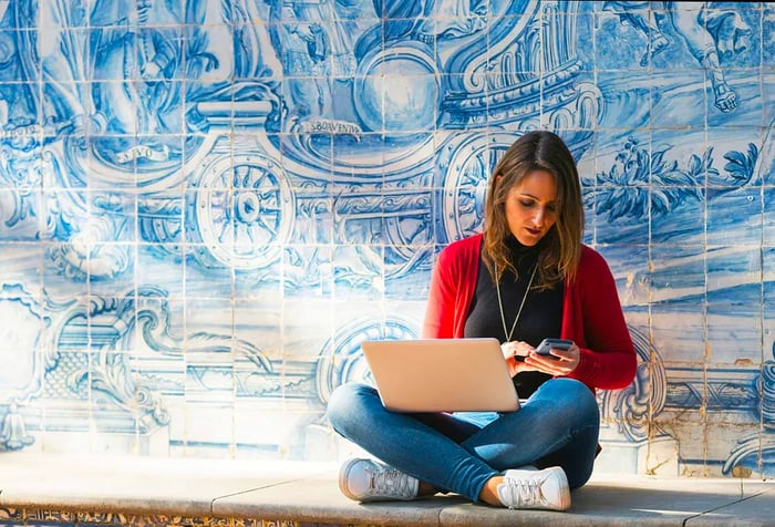 A woman working on her laptop and phone beside beautiful Portuguese tiles