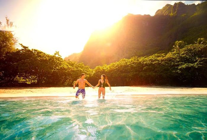 A man and a woman prepare to enter the water at a picturesque tropical beach.