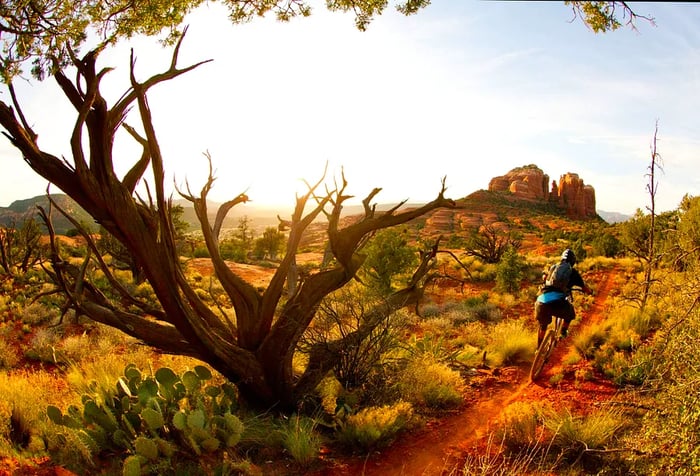 A male biker navigating a narrow trail across rugged hills, heading toward a towering rock formation.