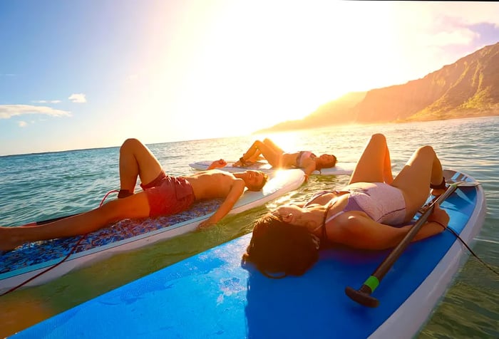 Three individuals relaxing on their backs atop a surfboard in the ocean.