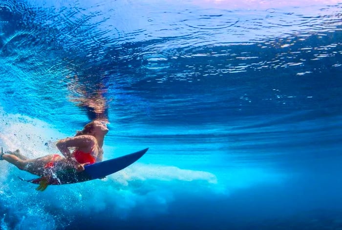 A woman in an orange bikini is immersed in the ocean while riding a wave on her surfboard.