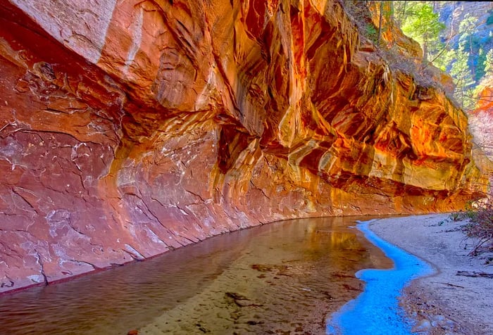 A beautifully carved rock wall looms over a gentle stream, showcasing wavy patterns.