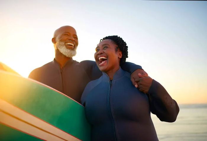 A couple joyfully carrying surfboards along the beach.