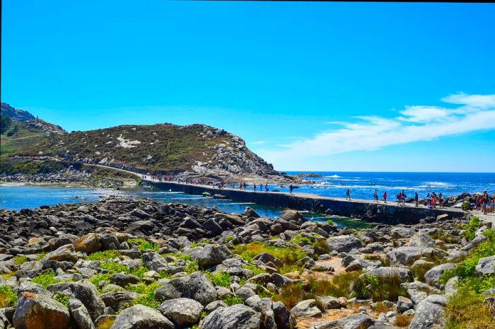 Visitors stroll along a walkway just above the water that connects two rocky islands.