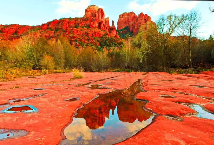 Reflective pools on sandstone rocks mirror the nearby jagged cliffs and steep rock formations.