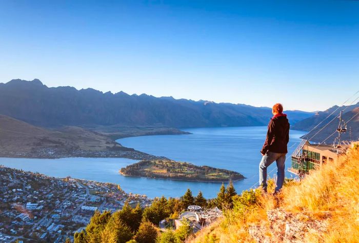 A hiker gazes at the stunning view of Queenstown during sunrise from a lookout point in Otago, New Zealand.