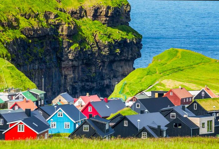 A quaint village adorned with colorful houses sits on the edge of a verdant gorge, overlooking the ocean.