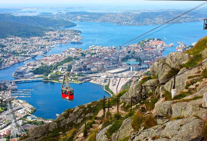 A striking red cable car gliding along a ropeway, offering breathtaking views of the sea and nearby towns.