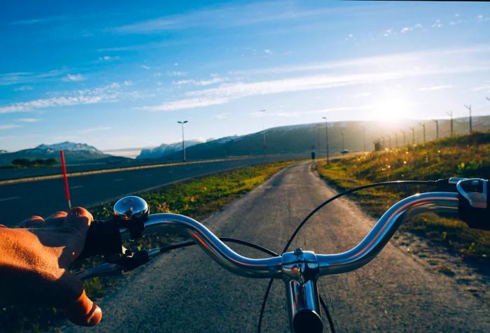 A cyclist rides along the dedicated bike path beside a wide highway on a bright, sunny day.