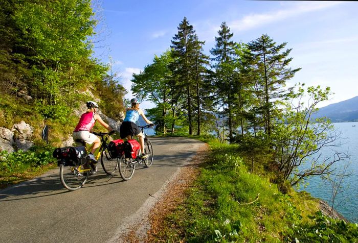 A couple cycling up a mountainous road with a lake in the background.