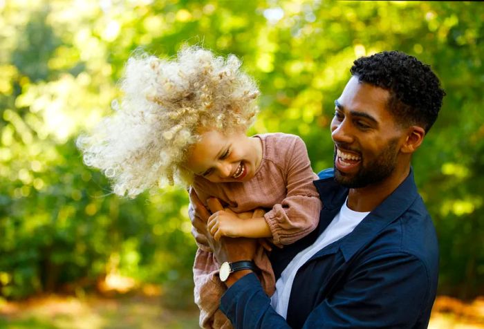 A father joyfully carries his lovely blonde-haired daughter in the park.