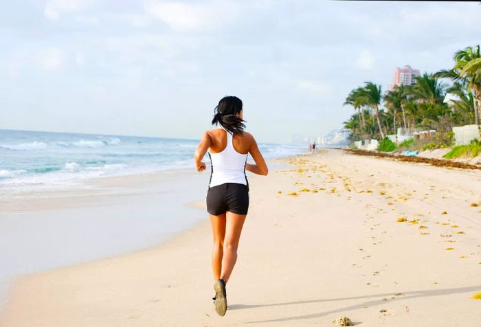 A woman in athletic wear jogs along a beach lined with palm trees.