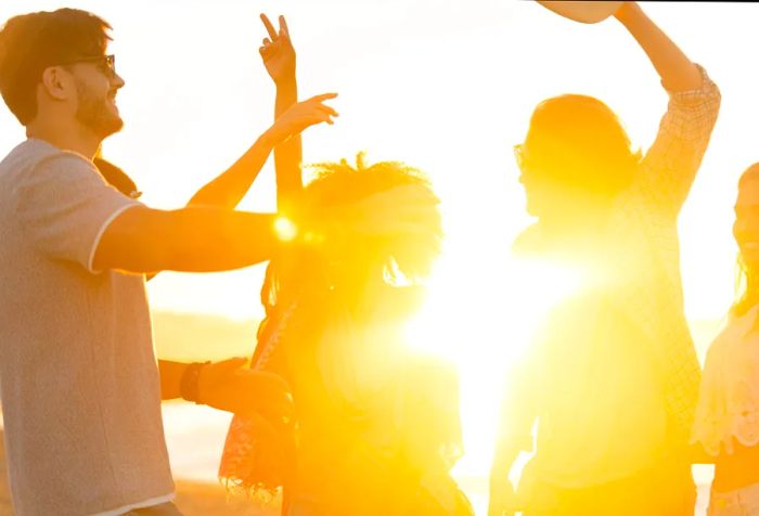 A group of young individuals dances and enjoys themselves on the beach at sunset.