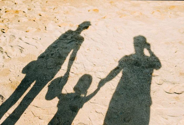 Three individuals holding hands create shadows on the sand.