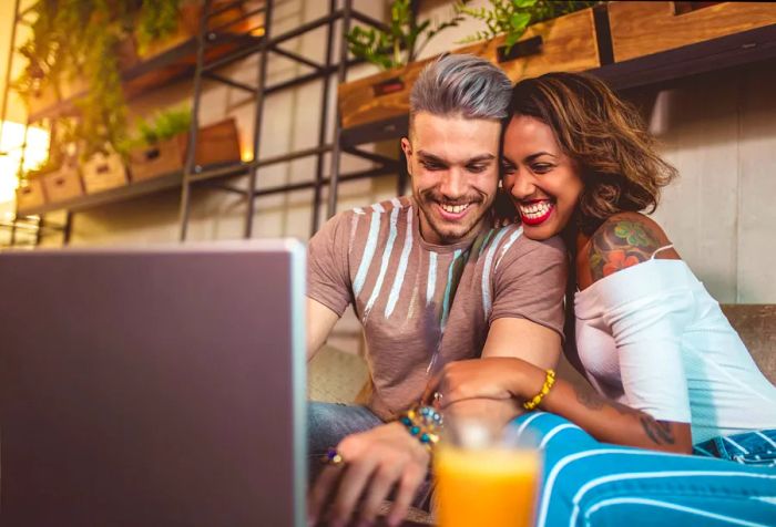 A joyful couple embraces while enjoying their time at a café with a laptop set before them.