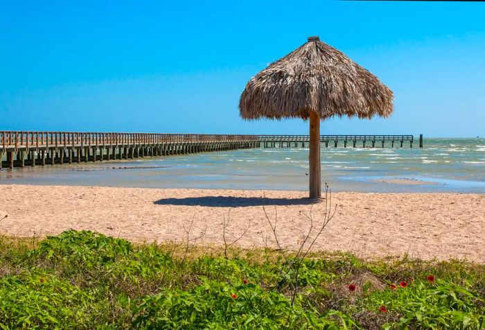 A beach featuring a lone thatched umbrella and an extensive pier extending into the water.